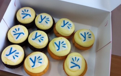 En æske med cupcakes, der hver har Yammers logo på glasuren.